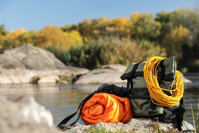 Photo of Set of camping equipment with sleeping bag on rock outdoors. Space for text