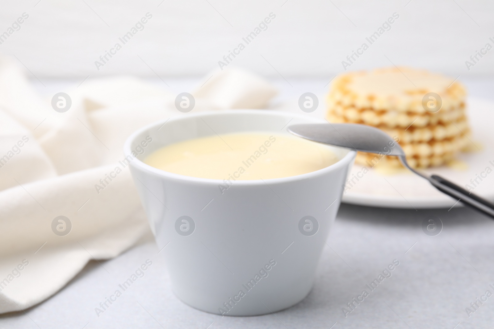 Tasty condensed milk in bowl and spoon on light grey table, closeup Photo of Tasty condensed milk in bowl and spoon on light grey table, closeup