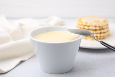 Photo of Tasty condensed milk in bowl and spoon on light grey table, closeup