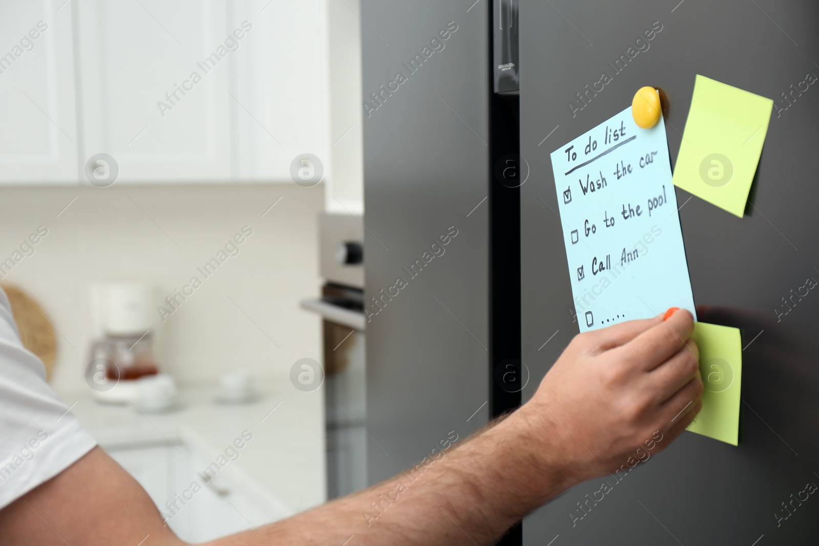 Photo of Man putting to do list on refrigerator door in kitchen, closeup