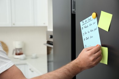 Photo of Man putting to do list on refrigerator door in kitchen, closeup