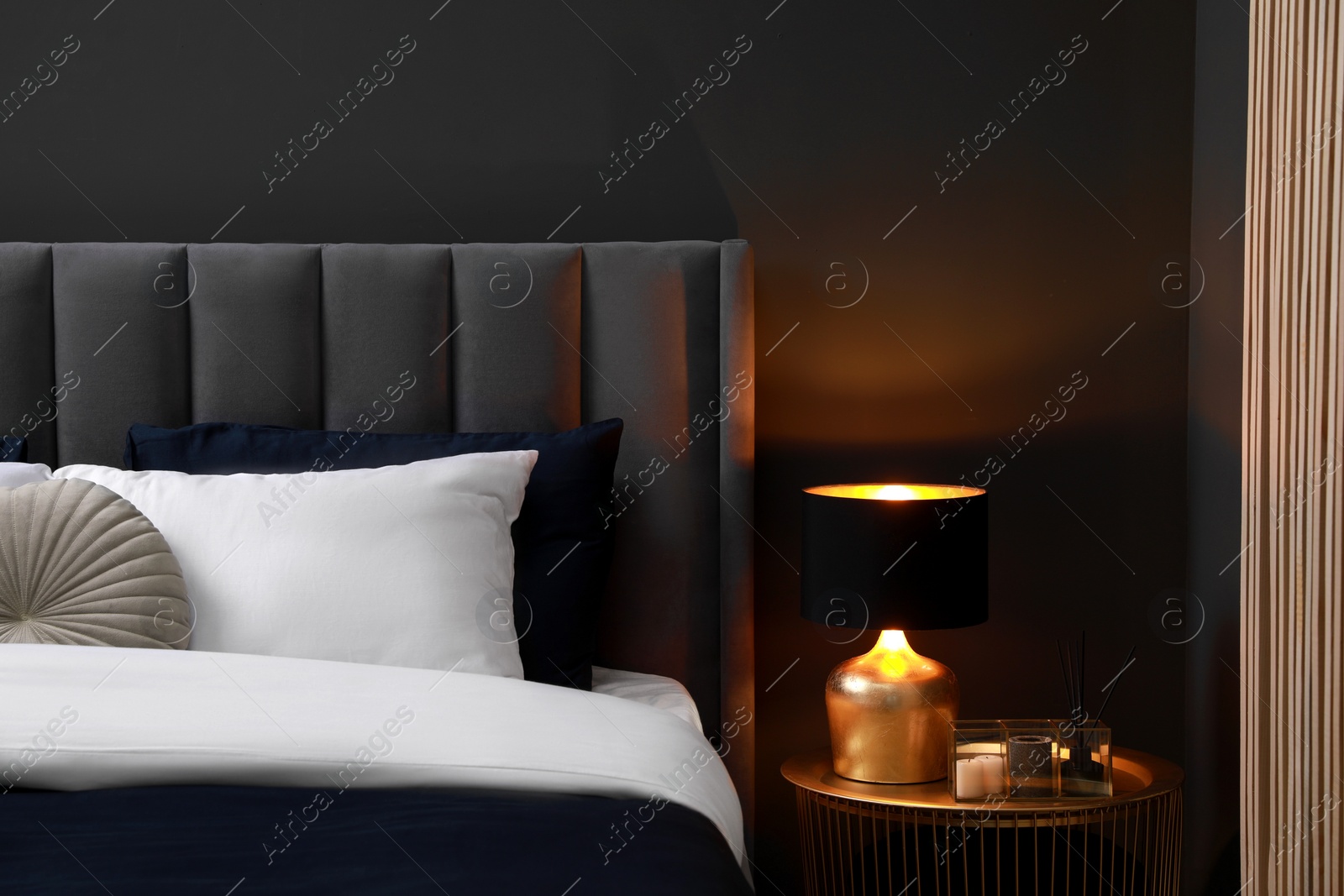 Photo of Comfortable bed with cushions, lamp and different decor on bedside table in room. Stylish interior