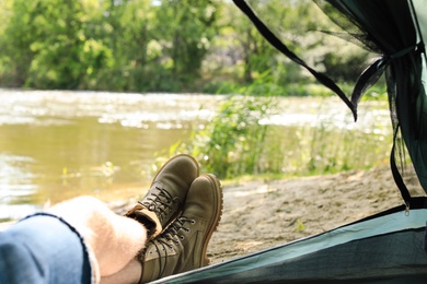 Photo of Young man resting in camping tent on riverbank, view from inside