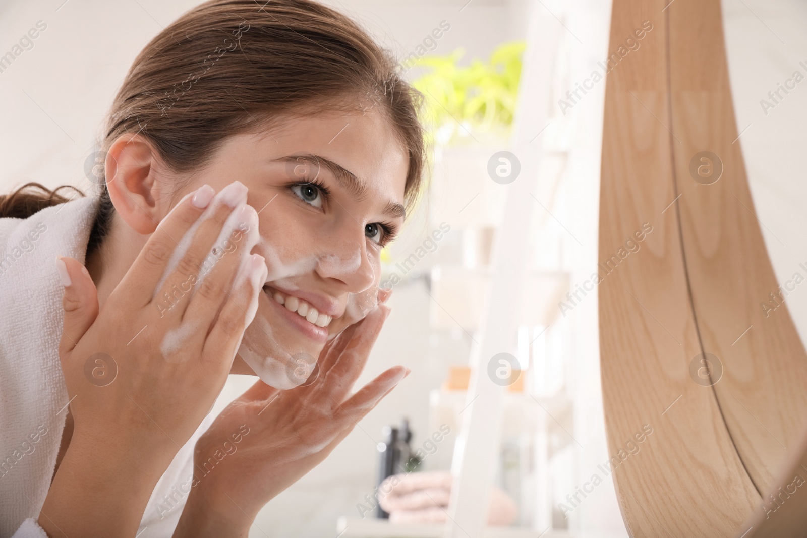 Photo of Beautiful teenage girl applying cleansing foam onto face in bathroom. Skin care cosmetic