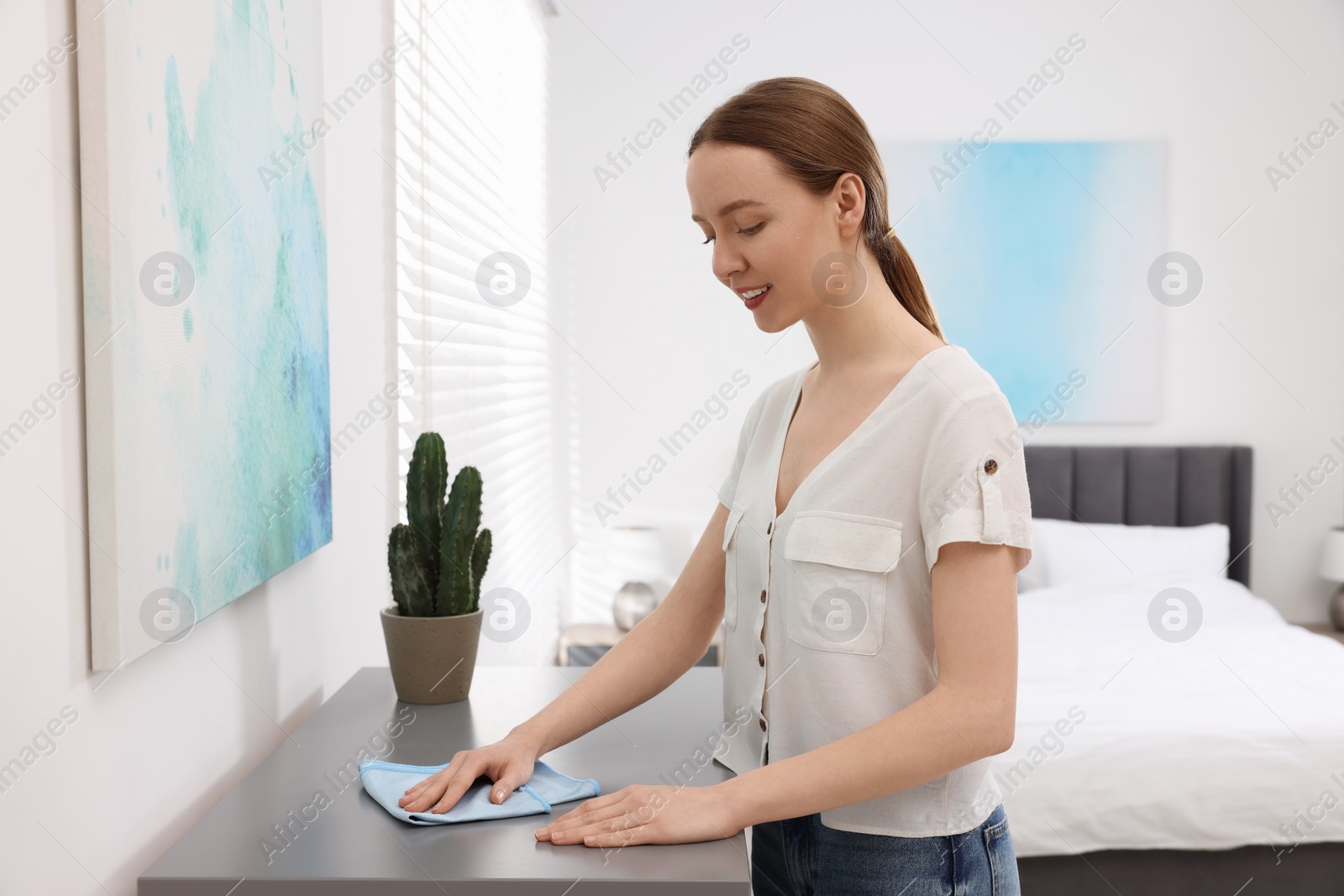 Photo of Woman with microfiber cloth cleaning grey chest of drawers in room