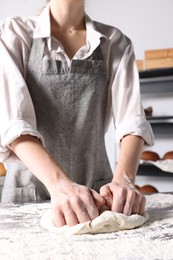 Photo of Woman kneading dough at table in kitchen, closeup