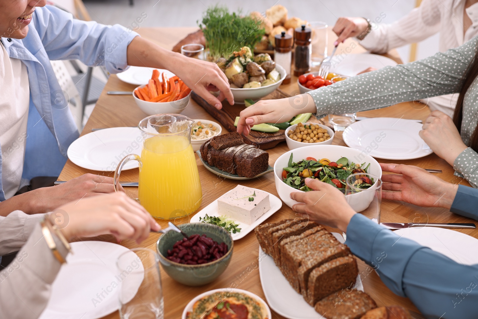 Photo of Friends eating vegetarian food at wooden table indoors, closeup