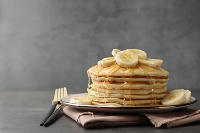 Photo of Tasty pancakes with sliced banana and honey served on gray table, space for text