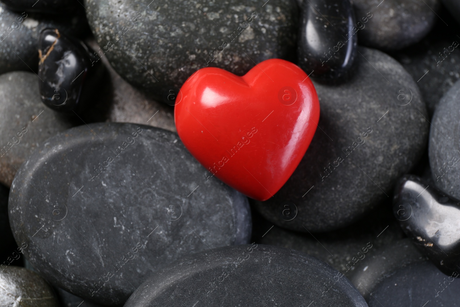 Photo of Red decorative heart on pebble stones, closeup