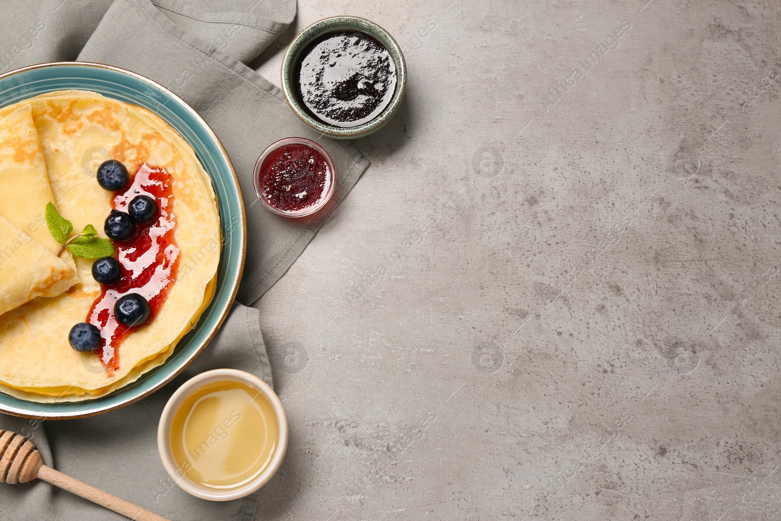 Photo of Delicious crepes with jam, honey and blueberries on light grey table, flat lay. Space for text