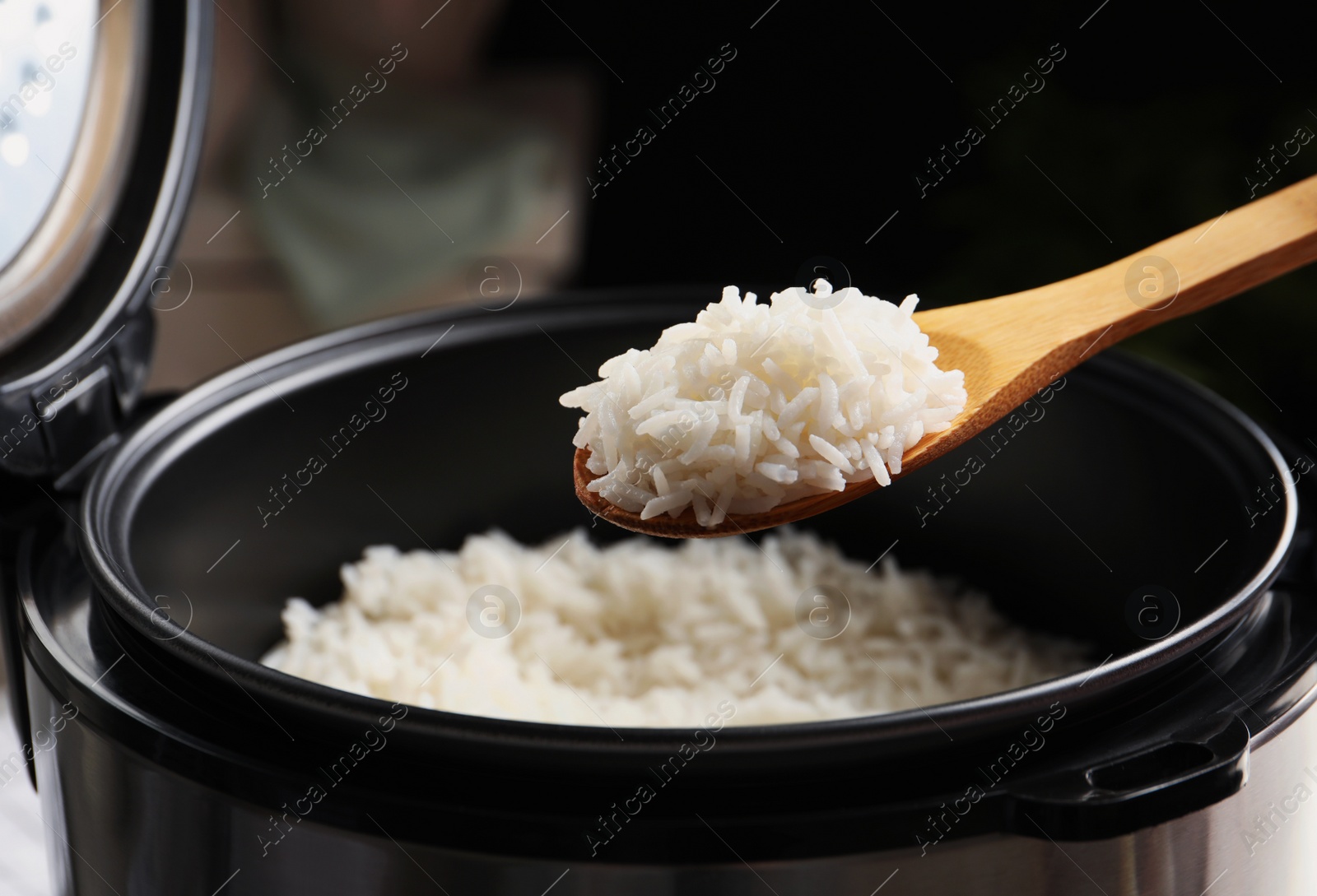 Photo of Spoon with tasty hot rice over cooker, closeup