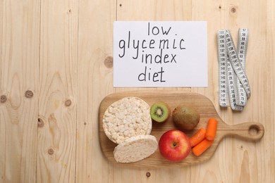 Photo of Paper with words Low Glycemic Index Diet, measuring tape and healthy products on wooden table, flat lay. Space for text