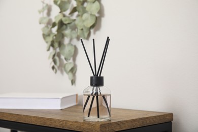 Reed diffuser and book on wooden table near white wall