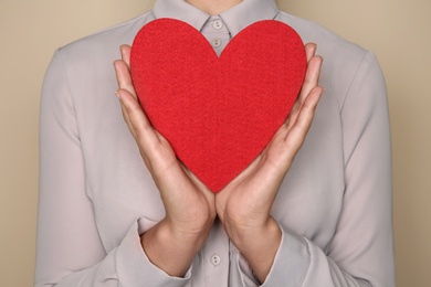 Young woman holding red heart on color background, closeup