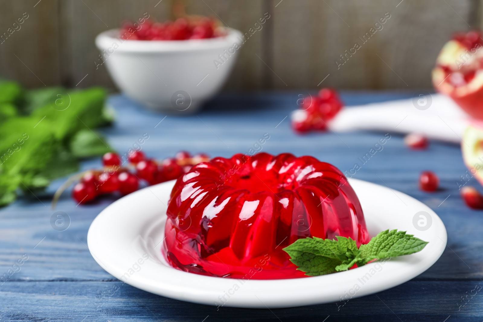 Photo of Delicious fresh red jelly with mint on blue wooden table