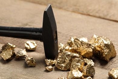 Pile of gold nuggets and hammer on wooden table, closeup
