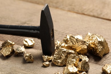 Photo of Pile of gold nuggets and hammer on wooden table, closeup