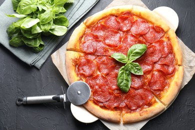 Tasty pepperoni pizza, cutter and basil on black textured table, flat lay