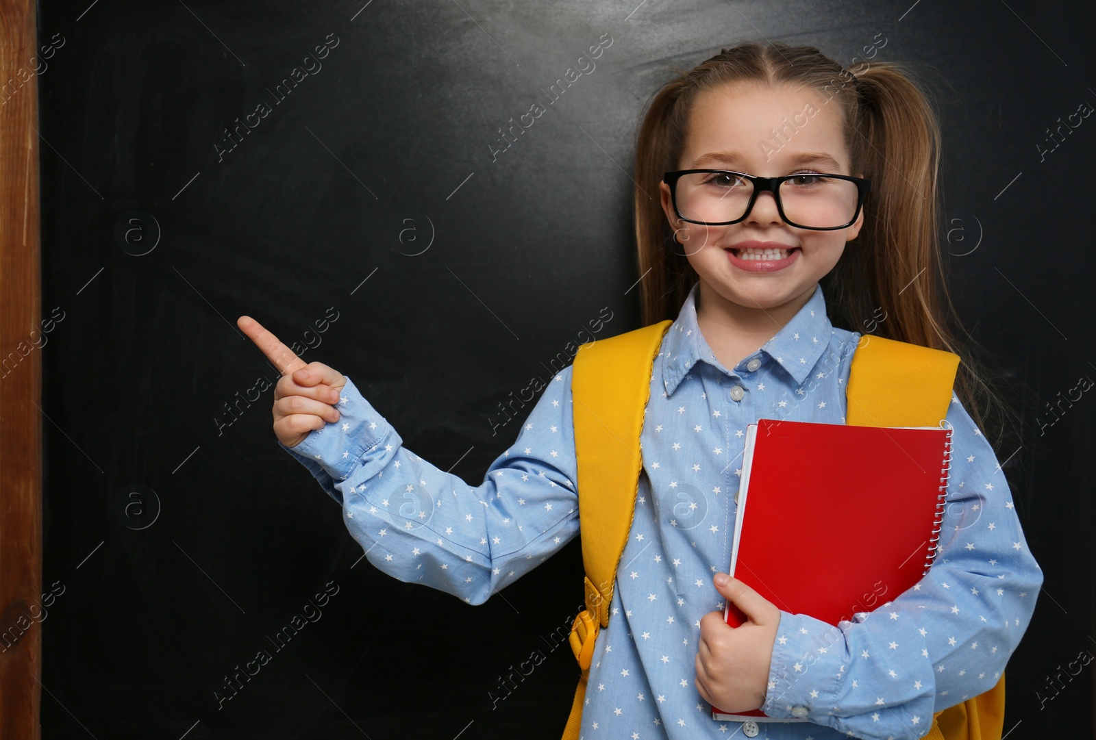 Photo of Cute little child wearing glasses near chalkboard. First time at school