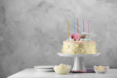 Photo of Delicious cake decorated with macarons, marshmallows and candles served on white table against grey background, space for text