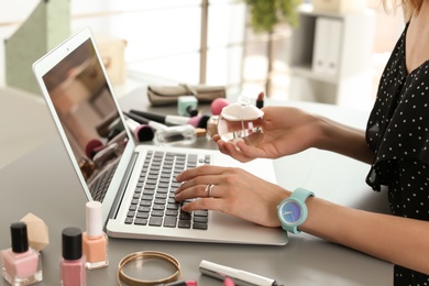 Young woman with makeup products using laptop at table. Beauty blogger