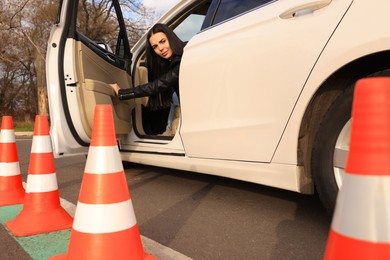 Photo of Young woman in car on test track with traffic cones, low angle view. Driving school