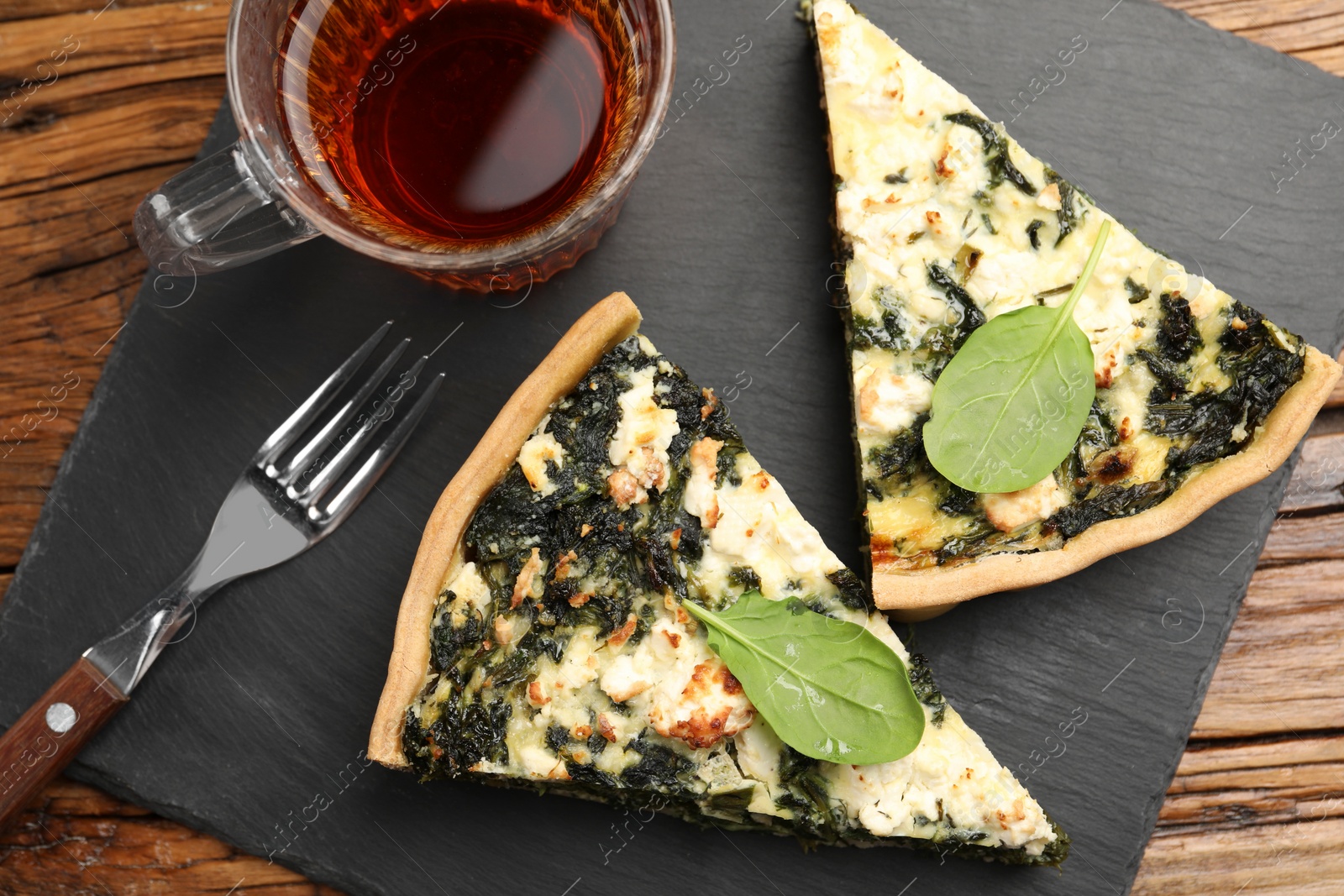 Photo of Pieces of delicious homemade spinach quiche, tea and fork on wooden table, flat lay