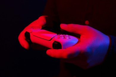 Man using wireless game controller on dark background in neon lights, closeup