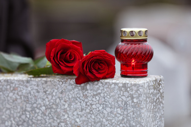 Photo of Red roses and candle on light grey tombstone outdoors. Funeral ceremony