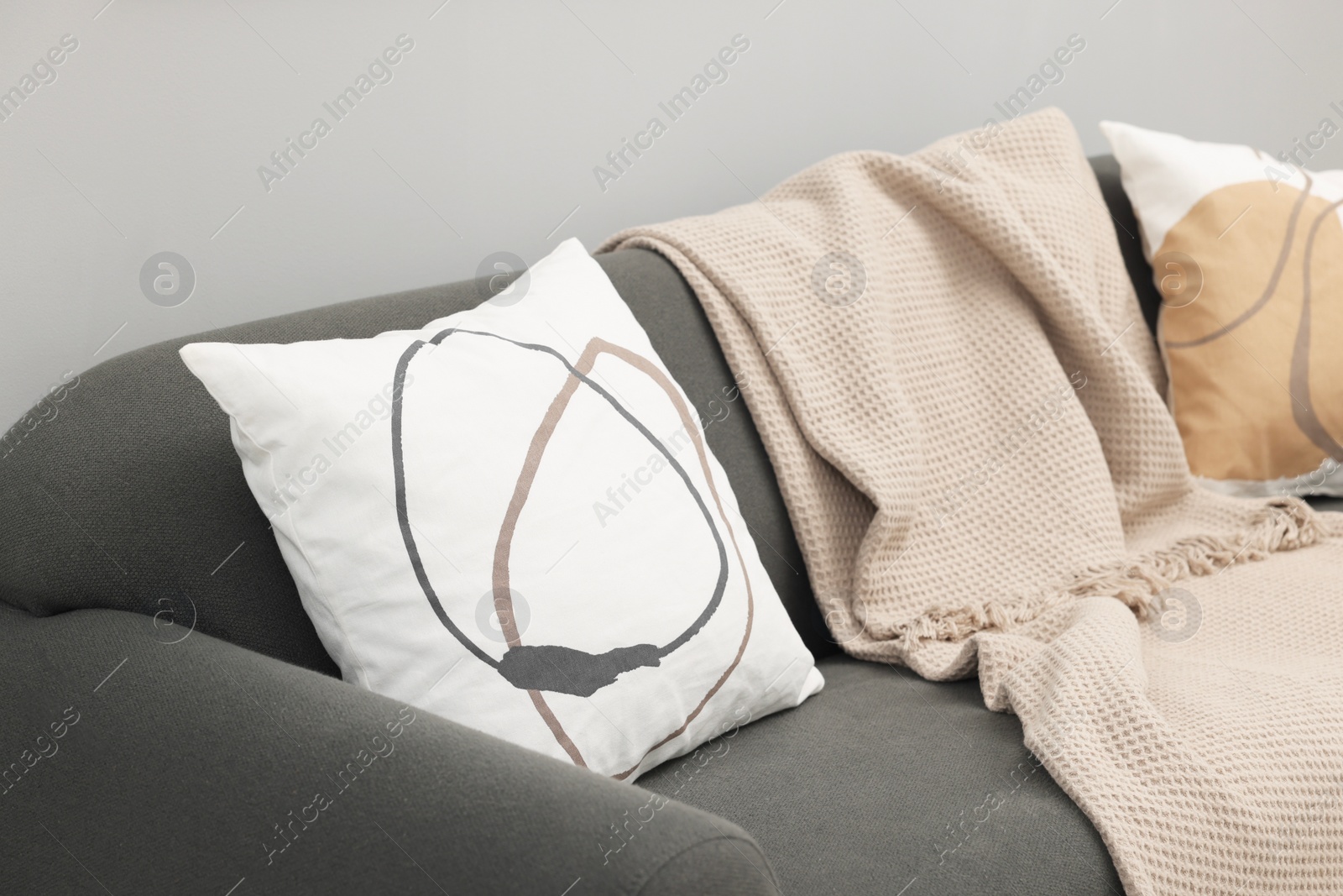 Photo of Soft pillows and blanket on sofa near grey wall indoors