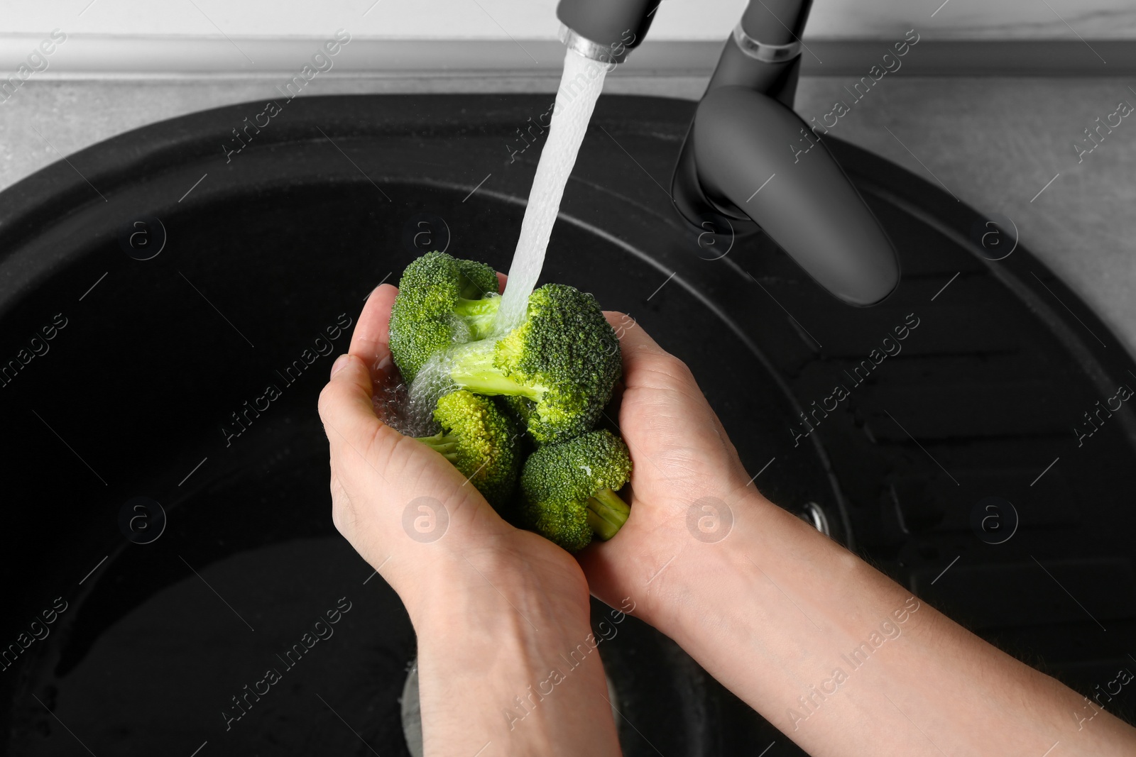 Photo of Woman washing fresh green broccoli in kitchen sink, closeup view