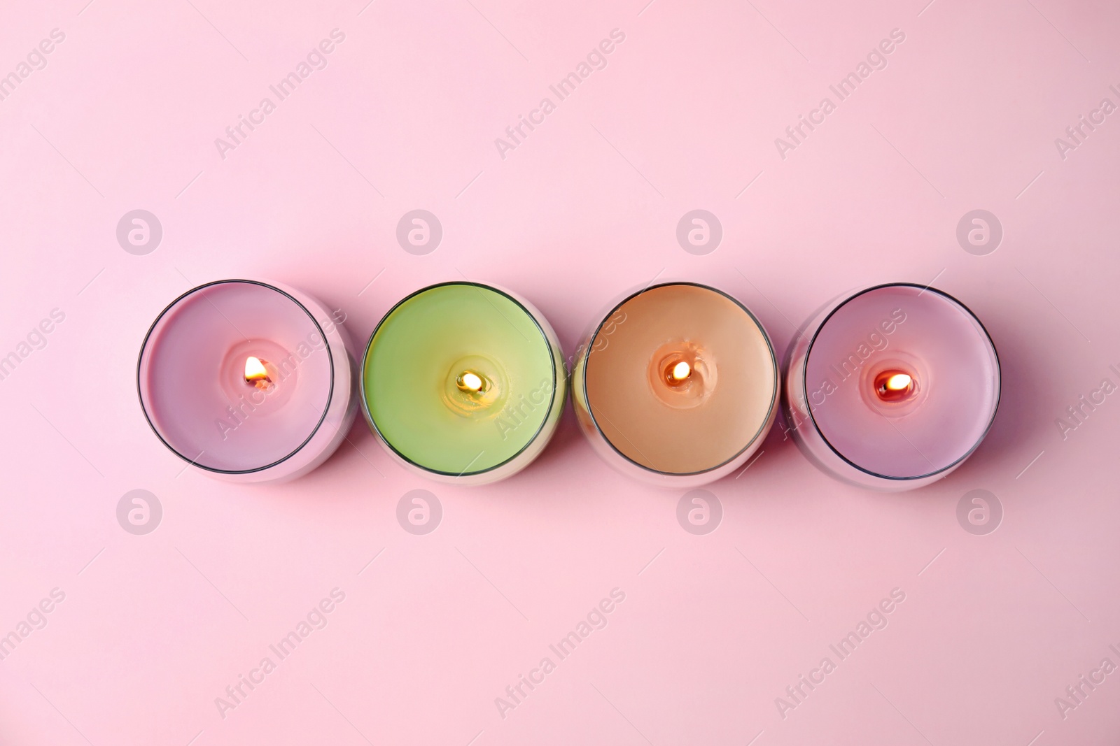 Photo of Burning wax candles in glass holders on pink background, flat lay