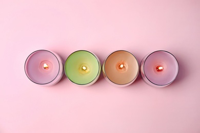 Photo of Burning wax candles in glass holders on pink background, flat lay