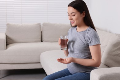 Photo of Pregnant woman with glass of water and pill at home, space for text