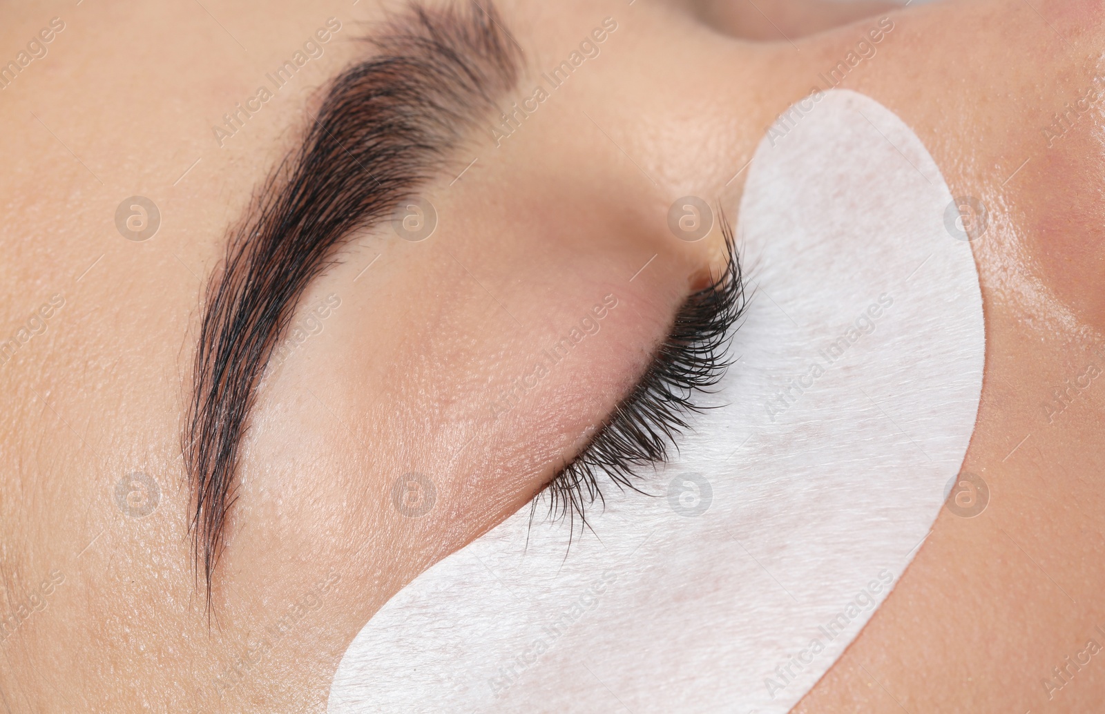 Photo of Young woman undergoing eyelashes extensions procedure, closeup