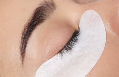 Young woman undergoing eyelashes extensions procedure, closeup