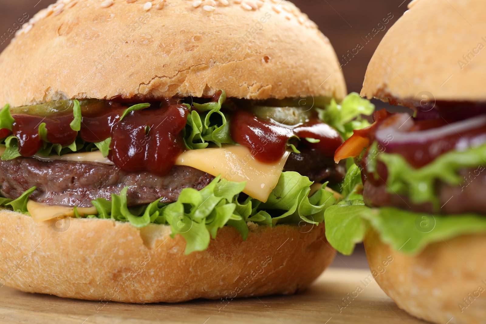 Photo of Delicious cheeseburgers with lettuce, pickle, ketchup and patty on wooden table, closeup