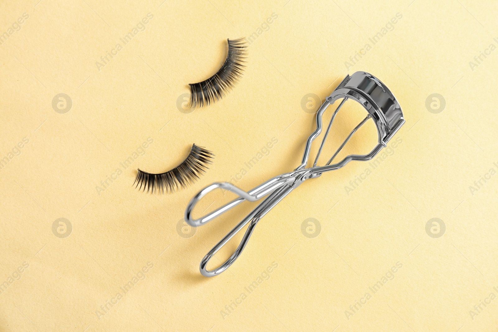 Photo of Curler and false eyelashes on color background, flat lay