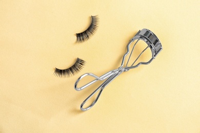 Photo of Curler and false eyelashes on color background, flat lay