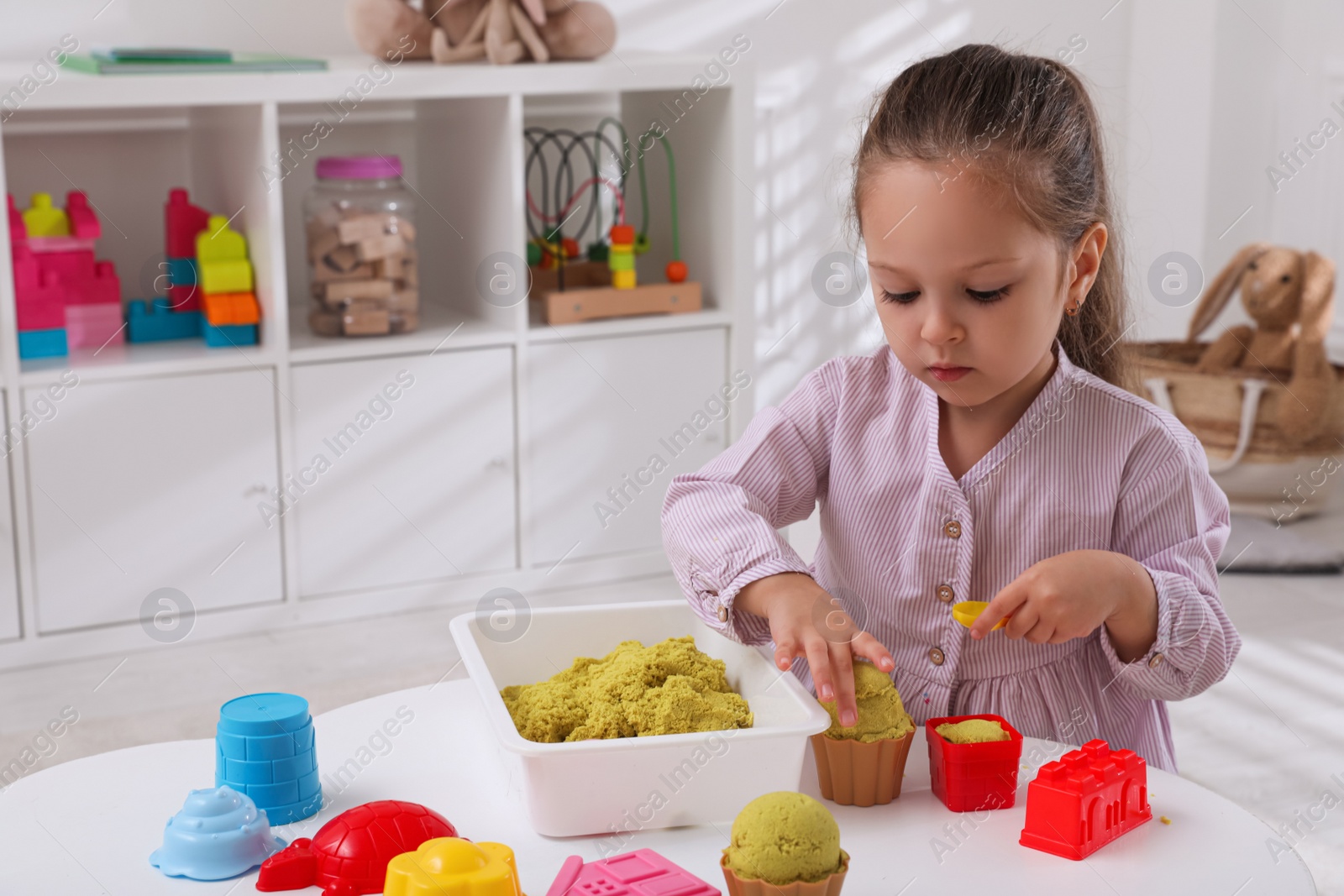 Photo of Cute little girl playing with bright kinetic sand at table in room