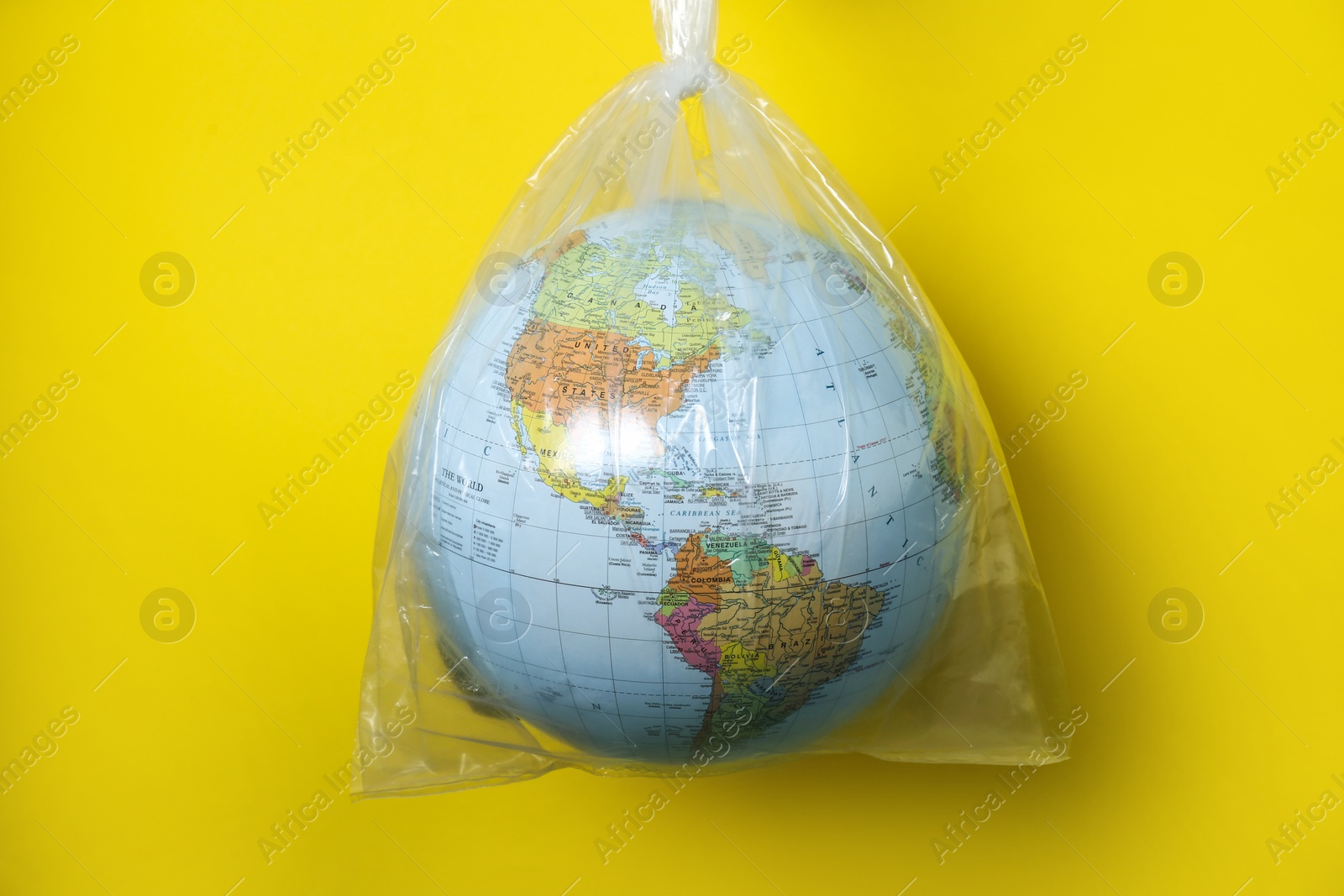 Photo of Globe in plastic bag hanging against yellow background. Environmental conservation