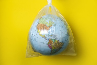 Photo of Globe in plastic bag hanging against yellow background. Environmental conservation