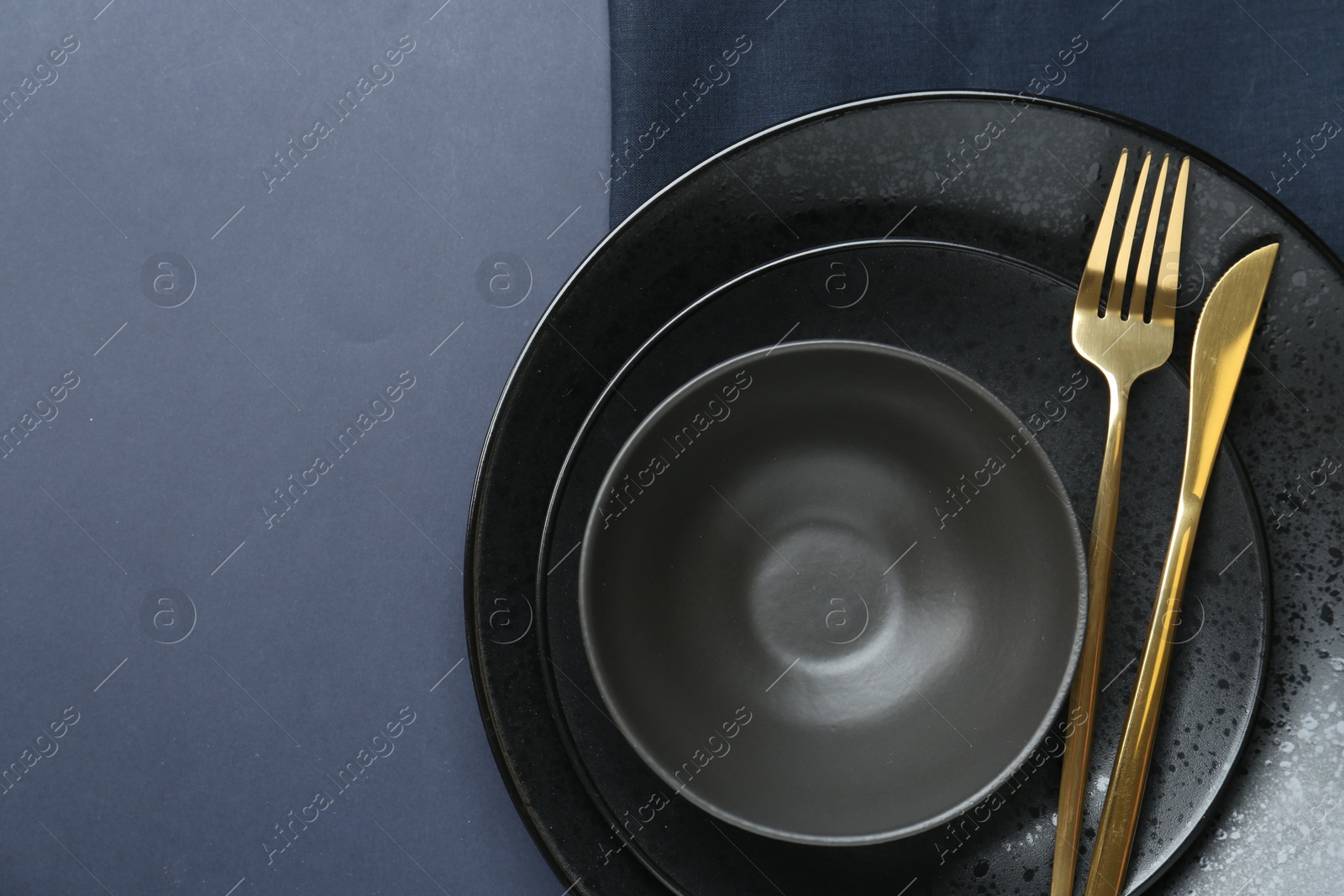 Photo of Stylish ceramic plates, bowl, cutlery and napkin on dark blue background, top view. Space for text