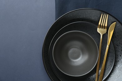 Stylish ceramic plates, bowl, cutlery and napkin on dark blue background, top view. Space for text