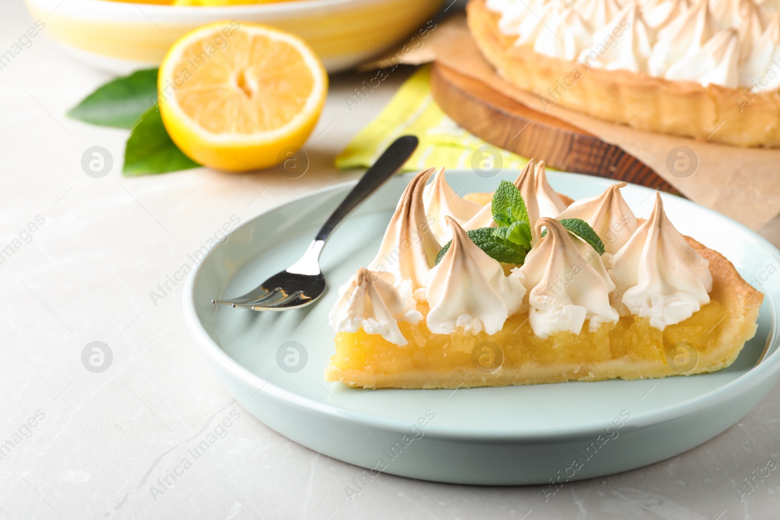 Photo of Piece of delicious lemon meringue pie with mint served on light table, closeup