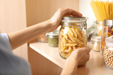 Photo of Woman taking jar of pasta from wooden shelf, closeup
