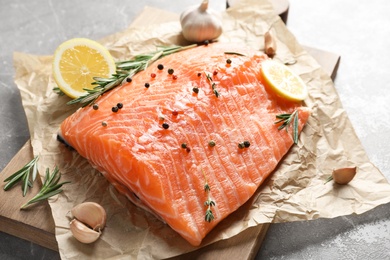 Wooden board with raw salmon and ingredients for marinade on grey background