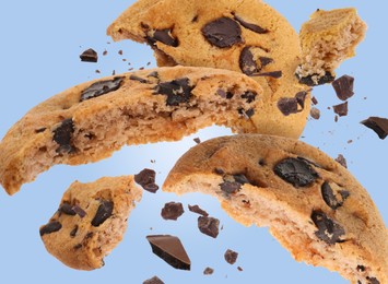 Tasty chocolate chip cookies falling on light blue background