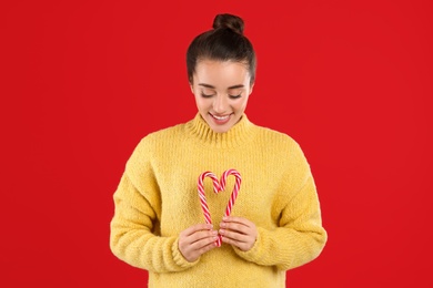 Photo of Young woman in yellow sweater holding candy canes on red background. Celebrating Christmas