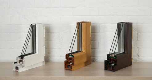 Photo of Samples of modern window profiles on table against brick wall. Installation service